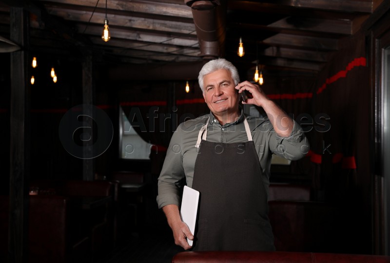 Senior business owner talking on phone in his restaurant