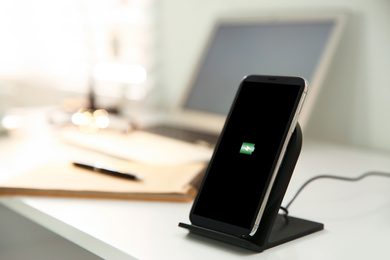 Mobile phone with wireless charger on white table. Modern workplace accessory