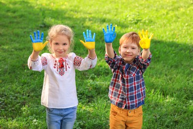 Photo of Little girl and boy with hands painted in Ukrainian flag colors outdoors. Love Ukraine concept