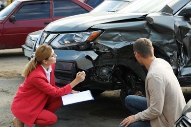 Man reporting and insurance agent filling claim form near broken car outdoors