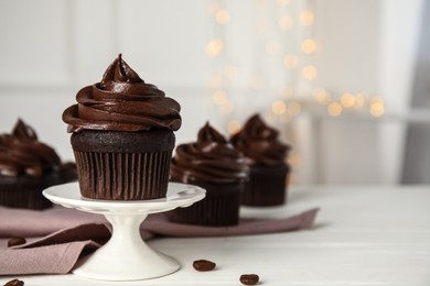 Dessert stand with delicious chocolate cupcake on white table against blurred lights. Space for text