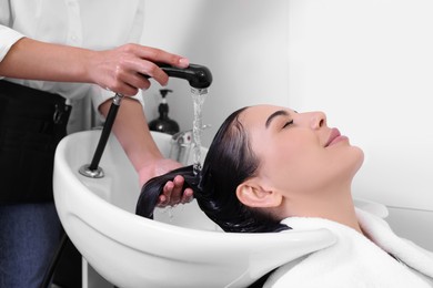 Professional hairdresser washing woman's hair in beauty salon, closeup