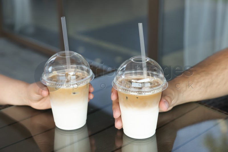 Man and woman with plastic takeaway cups of delicious iced coffee at table in outdoor cafe, closeup