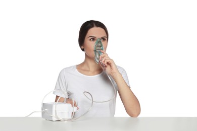 Young woman using nebulizer at table on white background