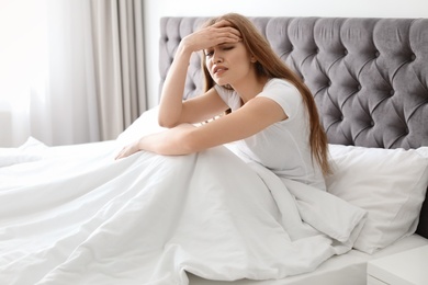 Young woman with terrible headache sitting in bed