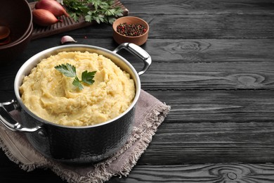 Photo of Pot of tasty mashed potatoes with parsley on black wooden table. Space for text