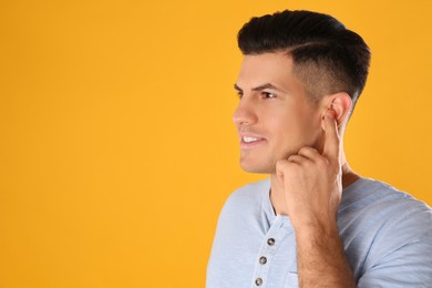 Man inserting foam ear plugs on yellow background. Space for text