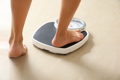 Woman stepping on floor scales indoors. Overweight problem