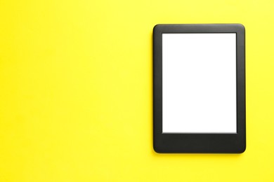 Modern e-book reader with blank screen on yellow background, top view. Space for text