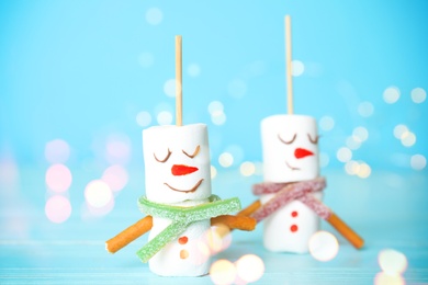 Funny snowmen made of marshmallows on light blue background, closeup. Bokeh effect 
