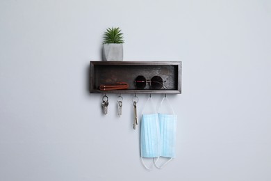 Wooden hanger for keys with wallet, sunglasses, medical masks and houseplant on white wall