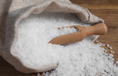 Bag of natural sea salt and scoop on wooden table, closeup