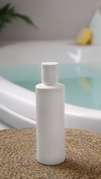 White bottle of bubble bath on wicker mat near tub indoors