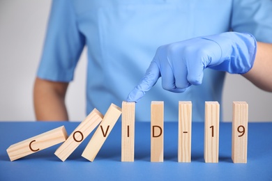 Doctor stopping domino effect at blue table, closeup. Prevent spreading of coronavirus