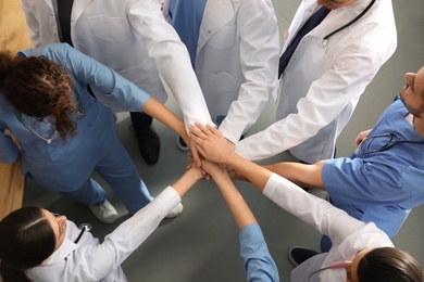 Team of medical workers holding hands together indoors, top view. Unity concept