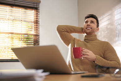 Young man with cup of drink relaxing at workplace