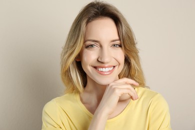 Portrait of happy young woman with beautiful blonde hair and charming smile on beige background