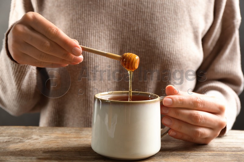Woman putting honey into tea at wooden table, closeup