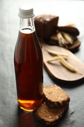 Photo of Bottle of delicious fresh kvass, spikelets and bread on grey table, closeup