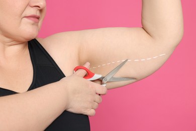 Obese woman with scissors on pink background, closeup. Weight loss surgery