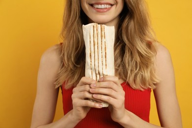 Photo of Young woman with delicious shawarma on yellow background, closeup