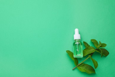 Photo of Bottle of essential oil and mint on green background, flat lay. Space for text