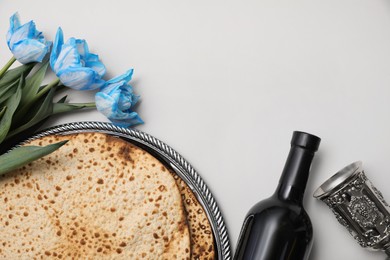 Tasty matzos, wine and tulips on light grey background, flat lay with space for text. Passover (Pesach) celebration