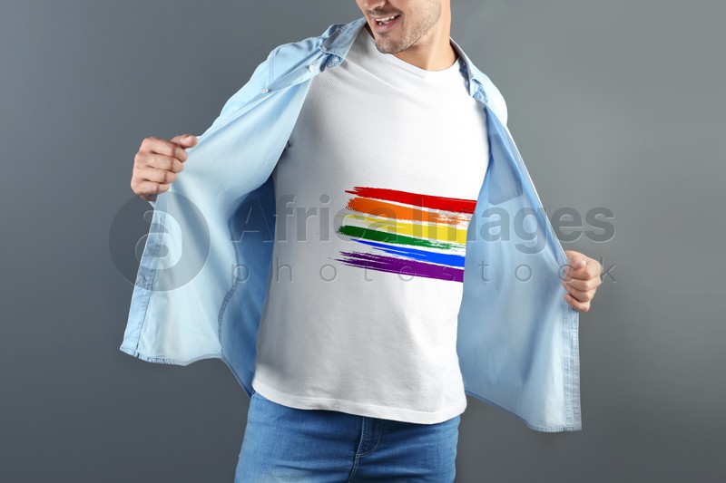 Young man white wearing t-shirt with image of LGBT pride flag on grey background