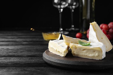 Tasty brie cheese with basil on black wooden table, space for text