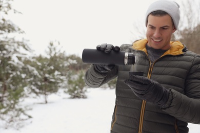 Man pouring hot drink from thermos into cap outdoors on snow day
