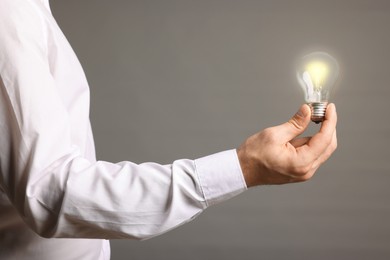 Glow up your ideas. Closeup view of man holding light bulb on grey background