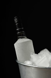 Bottle of vodka in metal bucket with ice on black background