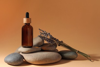 Bottle of face serum, spa stones and lavender flowers on beige background, space for text