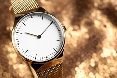 Photo of Luxury wrist watch on gold paillette background, closeup. Space for text
