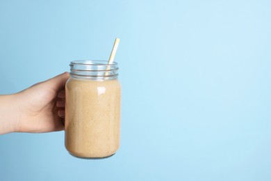 Photo of Woman holding mason jar with tasty smoothie and straw on light blue background, closeup. Space for text