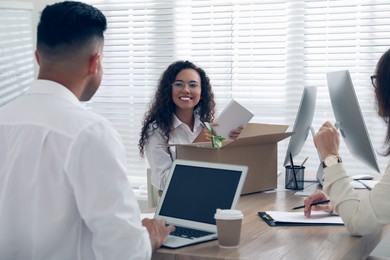 Photo of New employee unpacking box while talking with coworkers in office