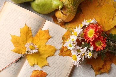 Photo of Book with leaves and beautiful flowers as bookmark on table, flat lay