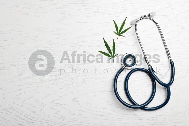Hemp leaves and stethoscope on white wooden background, flat lay. Space for text