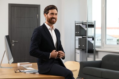 Smiling bearded man sitting on table in office