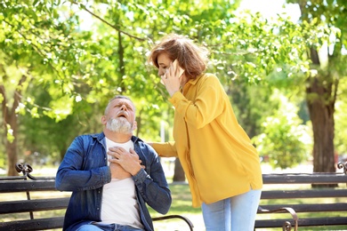 Woman calling ambulance for mature man having heart attack, outdoors