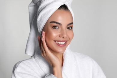 Beautiful young woman wearing bathrobe and towel on head against light background