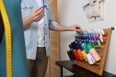 Photo of Dressmaker choosing thread of suitable color in workshop, closeup