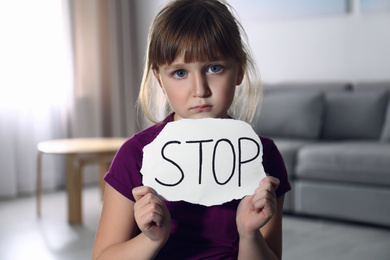 Abused little girl with sign STOP indoors. Domestic violence concept
