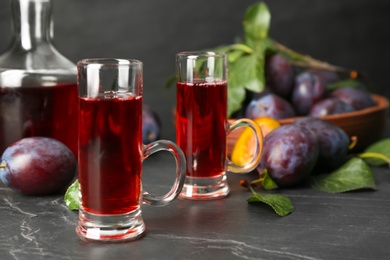 Photo of Delicious plum liquor and ripe fruits on black table. Homemade strong alcoholic beverage
