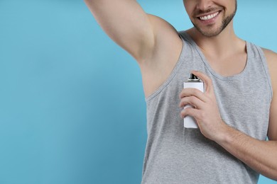 Man applying deodorant on turquoise background, closeup. Space for text