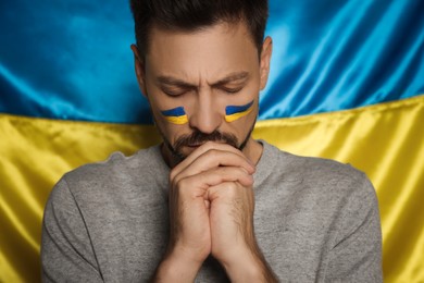Photo of Sad man with clasped hands near Ukrainian flag, closeup