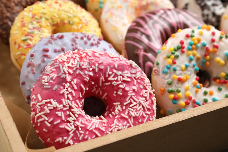 Photo of Yummy donuts with sprinkles in box, closeup
