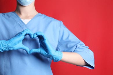 Doctor making heart with hands on red background, closeup