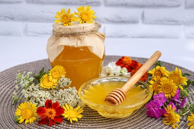 Delicious honey and different flowers on wicker mat against white brick wall