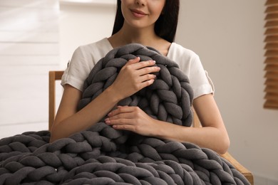 Photo of Woman with chunky knit blanket in armchair at home, closeup